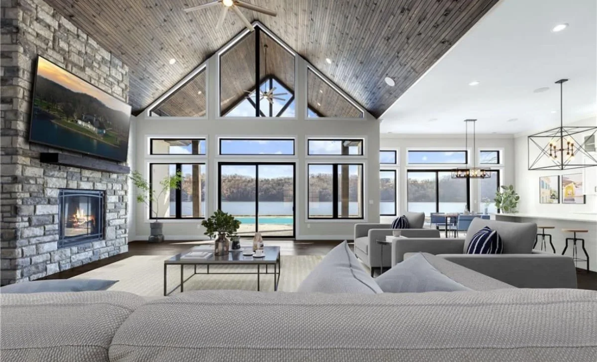 Living room with a stone fireplace, timber ceiling and tall windows facing the water.