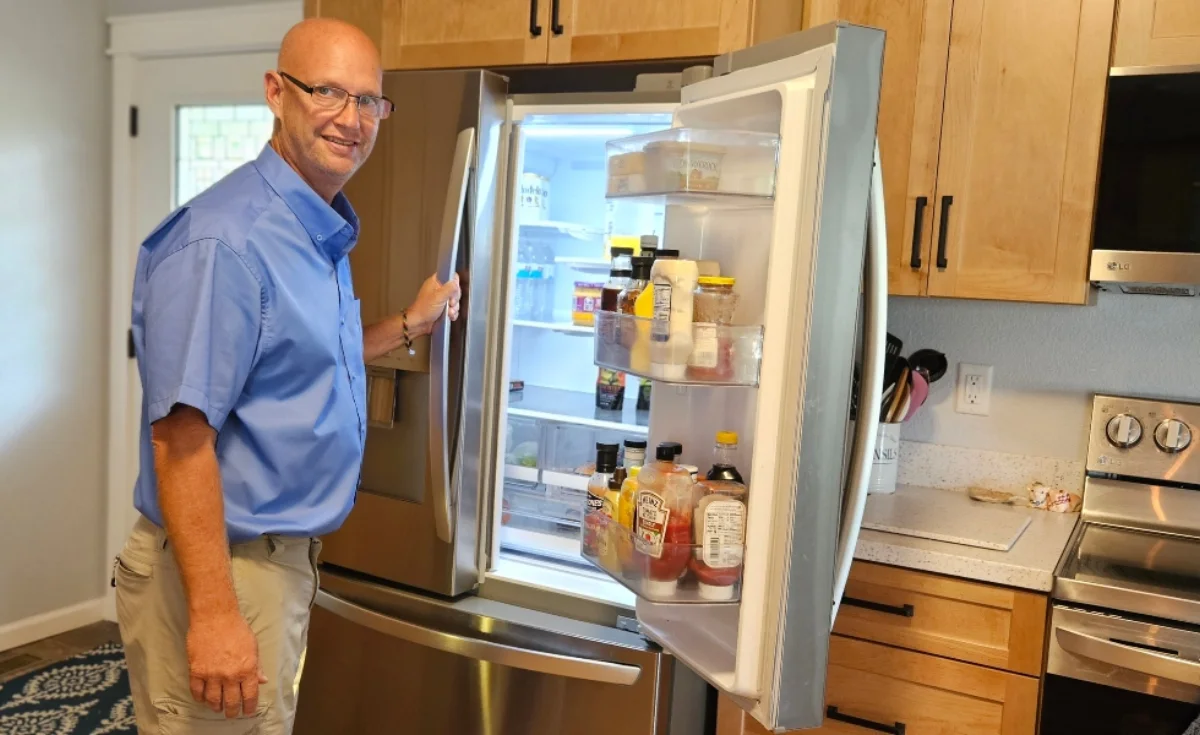 Person checking refrigerator shelves during a home-watch visit.