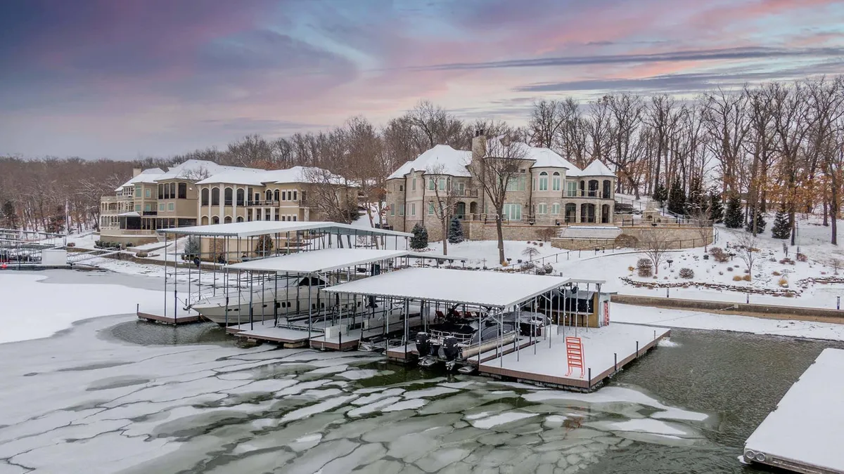 Snow-covered lakefront homes and covered boat docks on an icy lake at sunset.