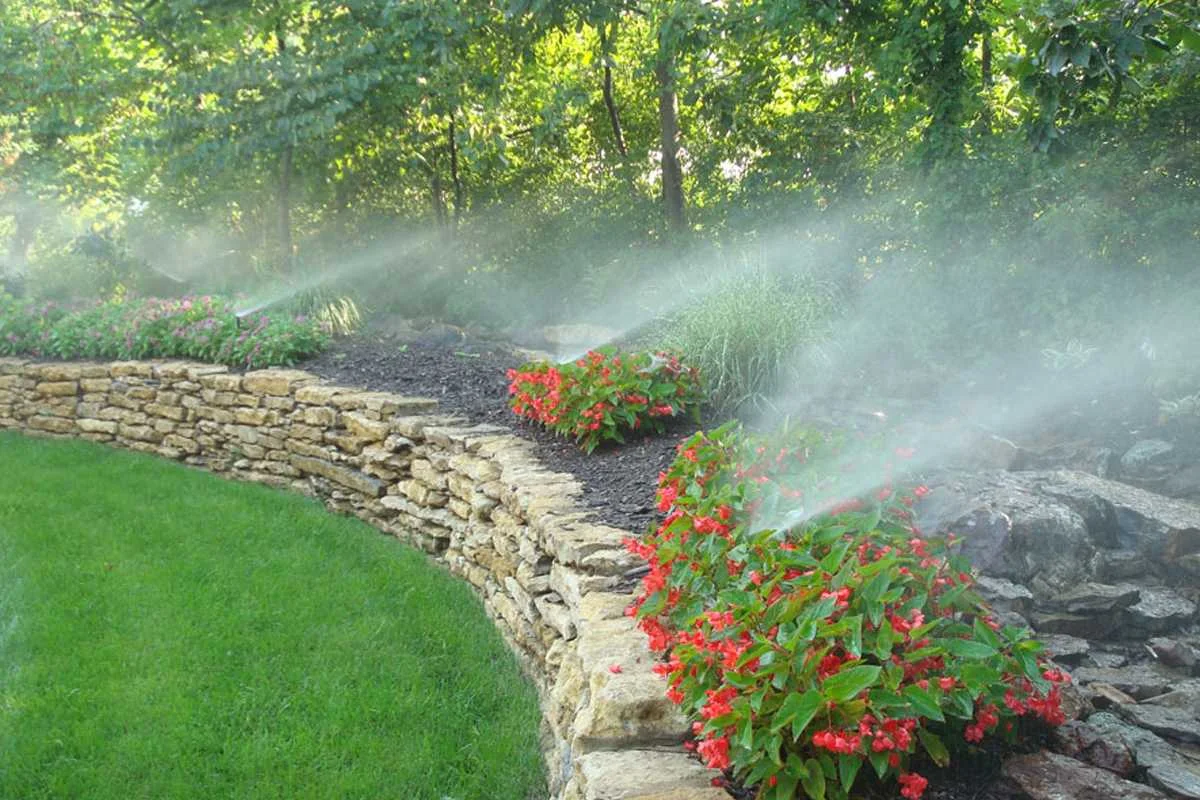 Sprinklers watering a landscaped garden and curved stone retaining wall.